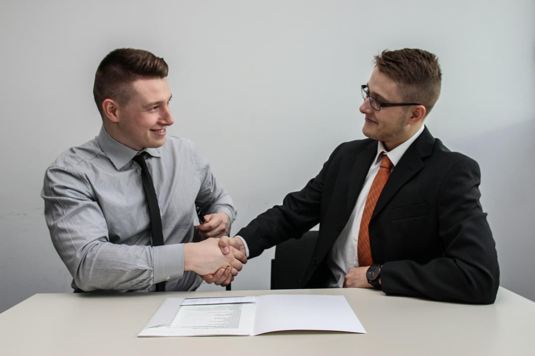 Two men facing each other while shaking hands and smiling