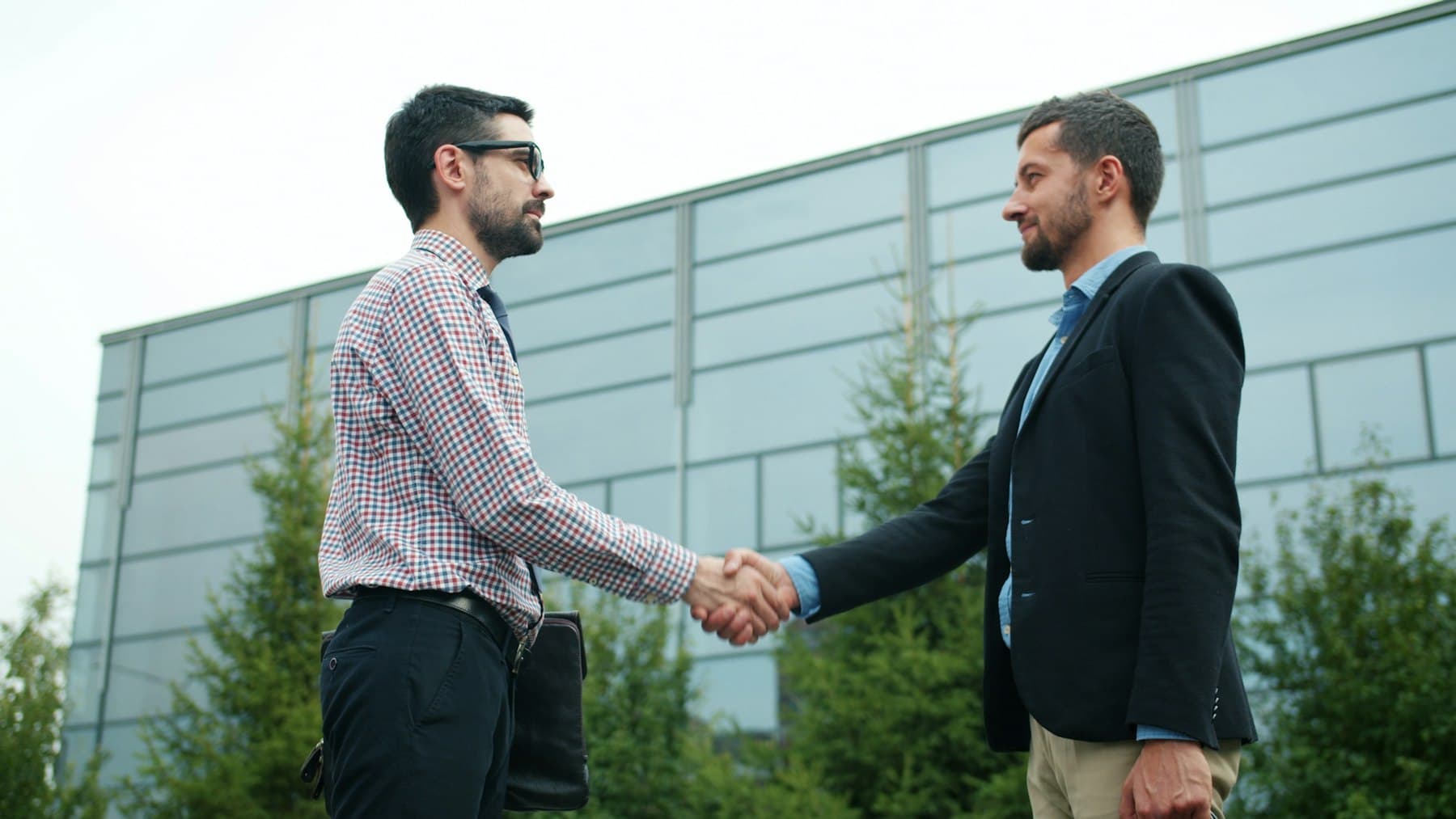 Two businesspeople shaking hands outside a modern office building